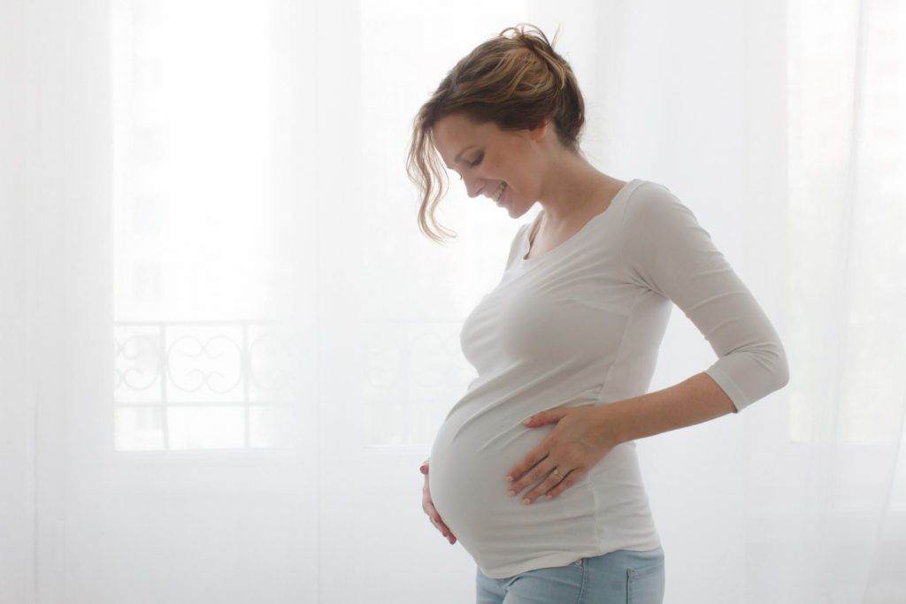 Mujer embarazada junto a una ventana con cortinas blancas