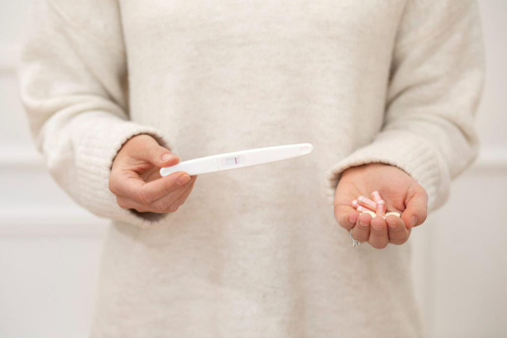 Mujer embarazadas con regla sosteniendo test de embarazo en la mano derecha y pastillas en la mano izquierda