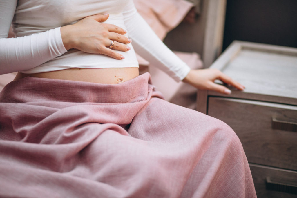 Mujer sentada en la cama apoyada en una mesilla sufriendo dolores de regla en embarazo