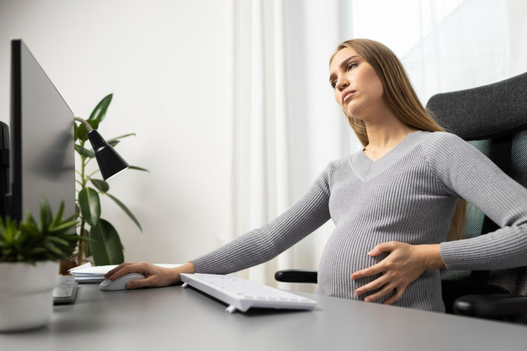 Mujer sentada delante del ordenador sufriendo dolores de regla en embarazo
