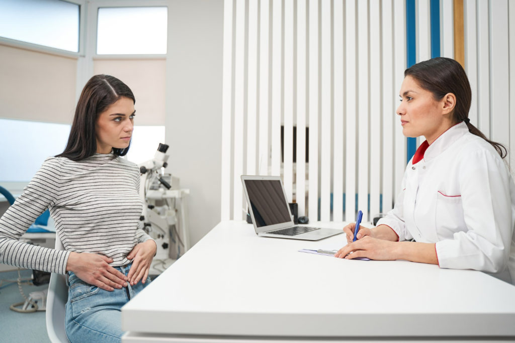 Mujer en consulta ginecologica tocando se la barriga y preguntando sobre congelar óvulos