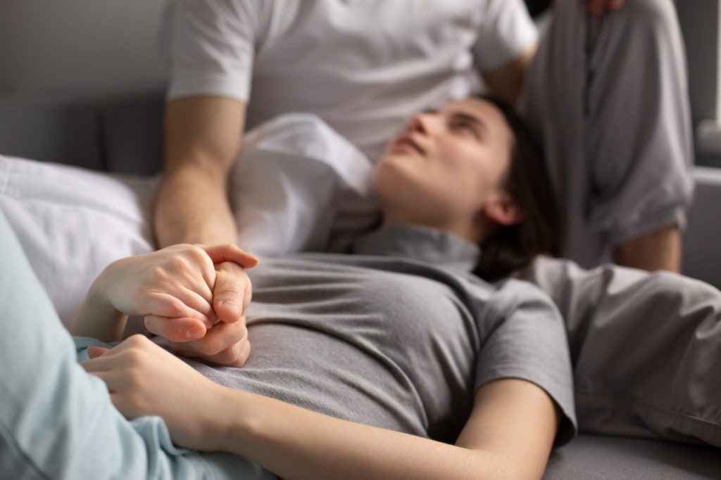Mujer acostada en reposo dándole la mano a su pareja después de hacerse un scratching endometrial.