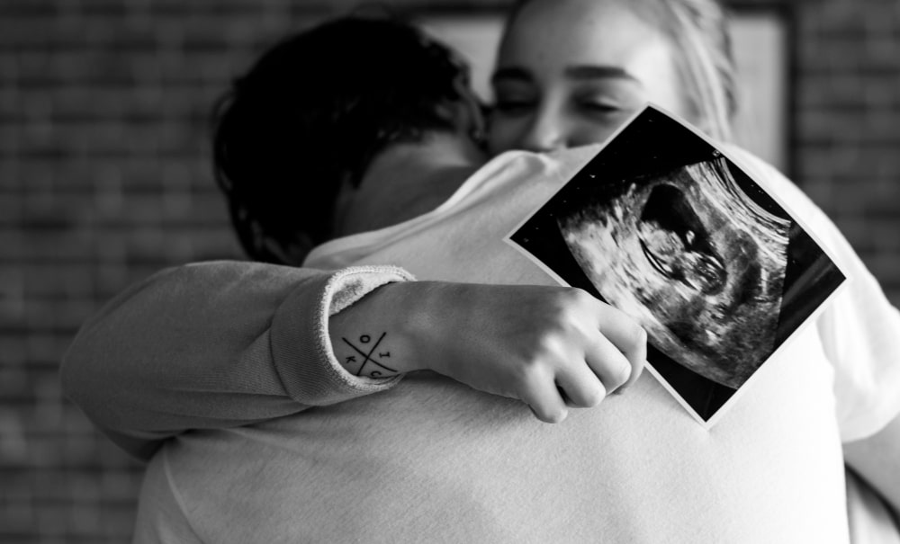 Mujer dandole un abrazo a su pareja sobre la ecografía de implantación del embrión