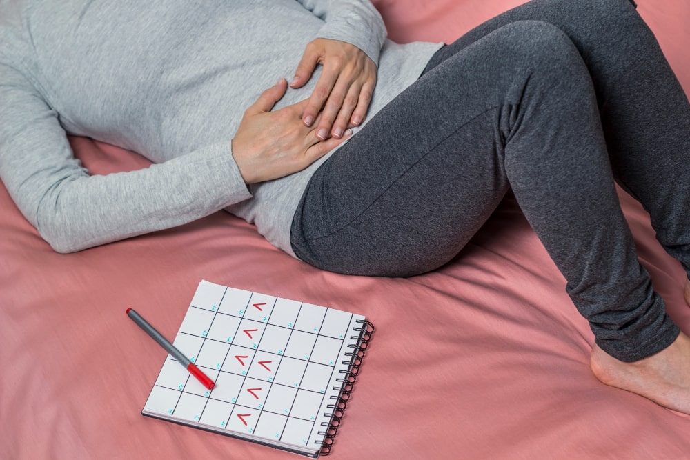 Mujer acostada el cama comprobando los días de regla por lo síntomas de embarazo a los 7 días