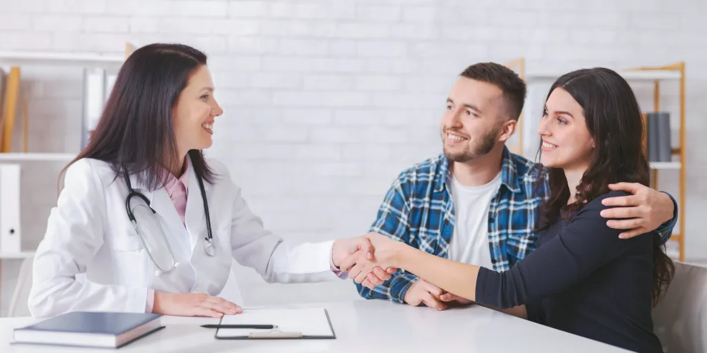 una-pareja-se-sienta-en-una-oficina-y-estrecha-la-mano-con-una-doctora-con-una-bata-blanca-todos-son-min Primera consulta gratuita clínica de fertilidad